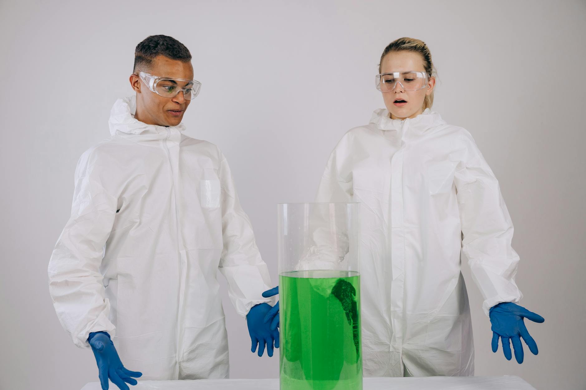 Dwaj chemicy w odzieży ochronnej obserwują zieloną reakcję w laboratorium