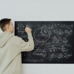Nastolatek w bluzie zapisuje wzory na tablicy podczas nauki chemii