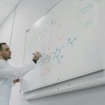 Nauczyciel tłumaczy równanie chemiczne na białej tablicy w klasie