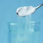 Wsypywanie cukru do szklanki z wodą na niebieskim tle