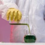 Chemik w rękawicach przelewa zielony roztwór w laboratorium