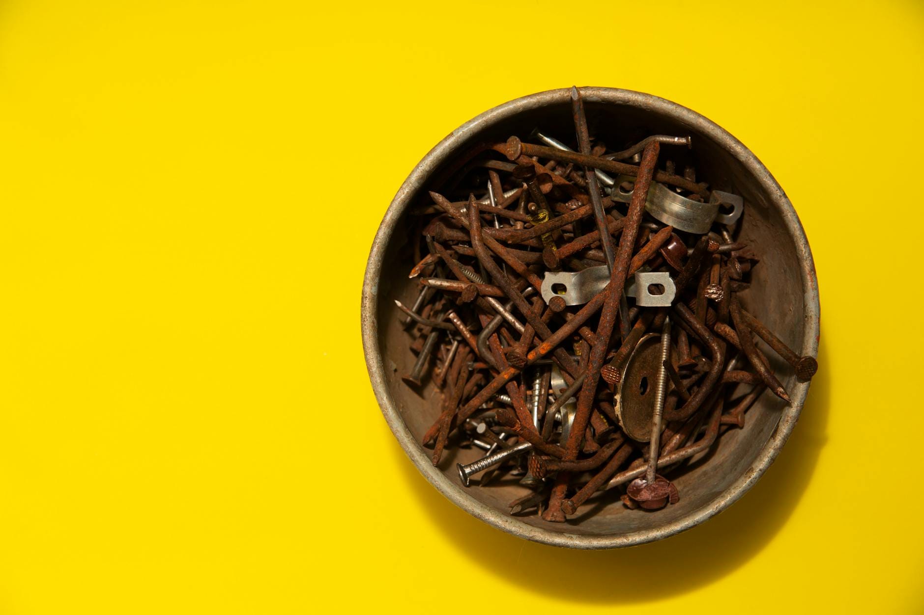 Miska z pordzewiałymi gwoździami na żółtym tle, widok z góry