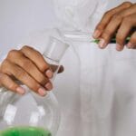 Naukowiec przelewa zielony roztwór między kolbami w laboratorium