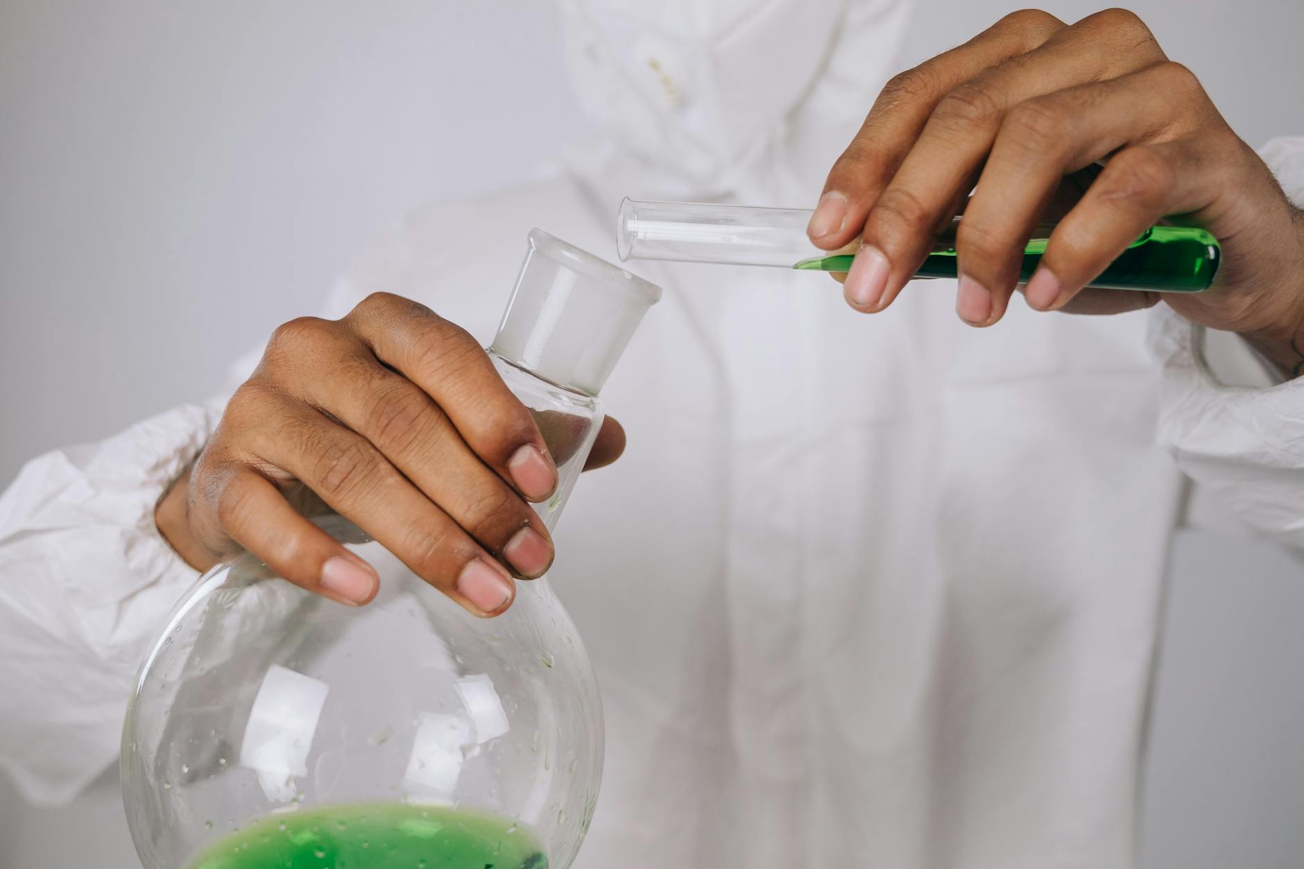 Naukowiec przelewa zielony roztwór między kolbami w laboratorium