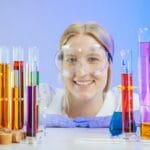Uśmiechnięta chemiczka z kolorowymi roztworami w szkle laboratoryjnym