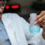 Młody chemik zbliżeniowo obserwuje reakcję chemiczną w szkolnym laboratorium