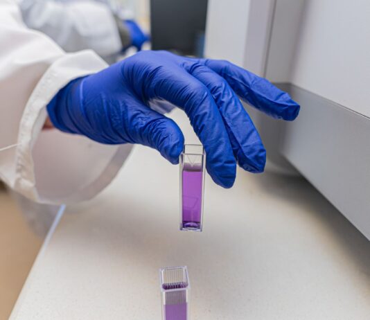 Kuwety spektrofotometryczne: kwarcowe, szklane czy z tworzywa – jak dobrać do pomiaru UV-Vis? Dłoń w rękawiczce trzyma fiolkę z fioletowym roztworem laboratoryjnym
