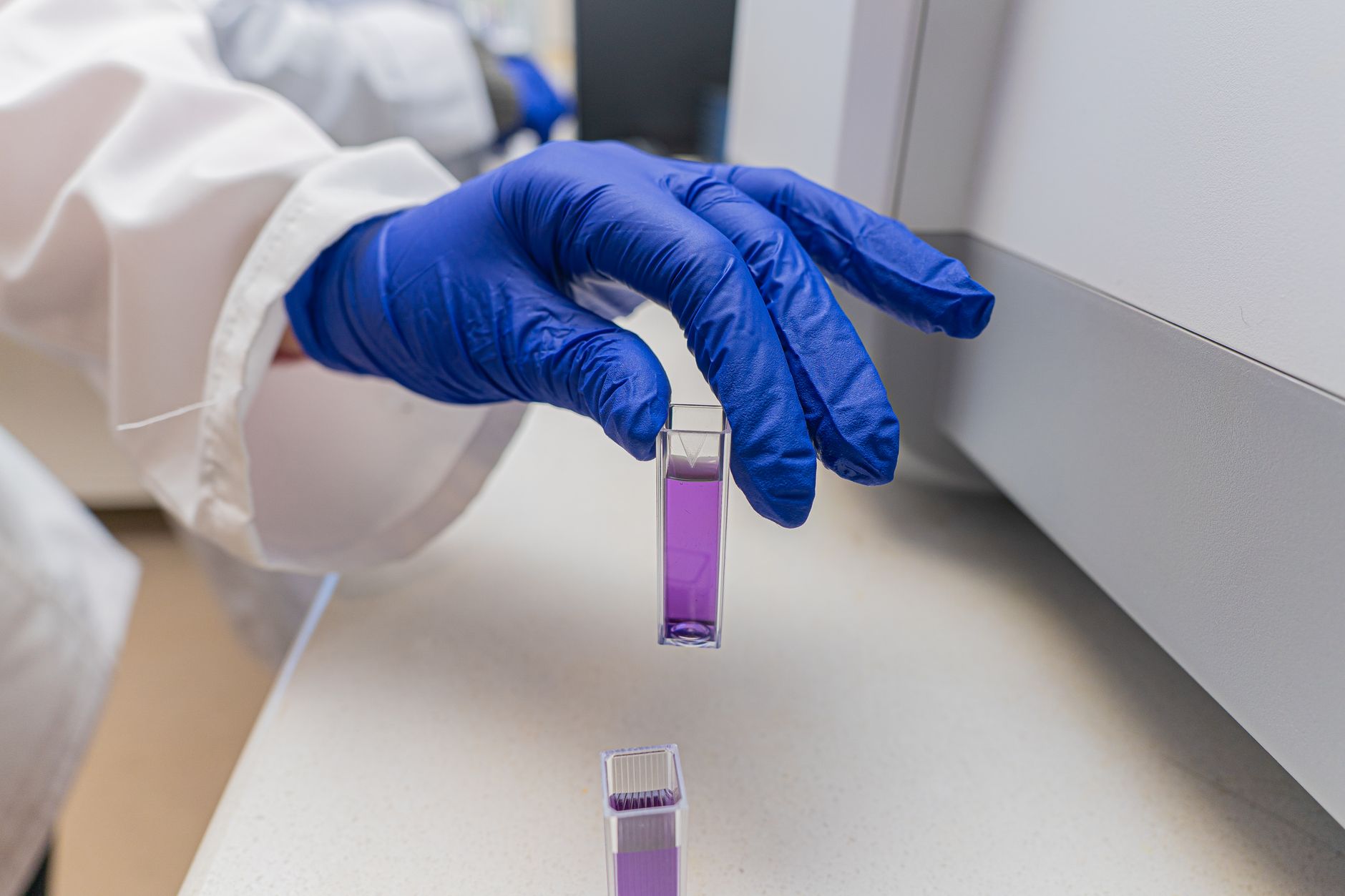 Dłoń w rękawiczce trzyma fiolkę z fioletowym roztworem laboratoryjnym